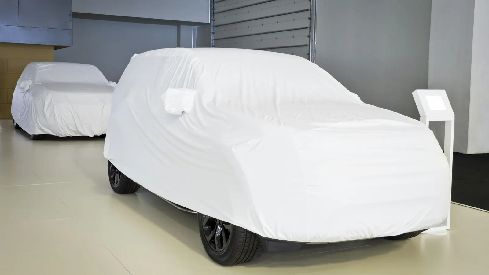 Two cars under white breathable covers in a clean indoor storage facility
